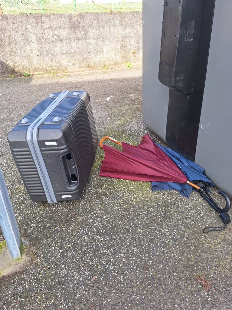Two broken umbrellas and a suitcase because Galicia is traveling and rain.